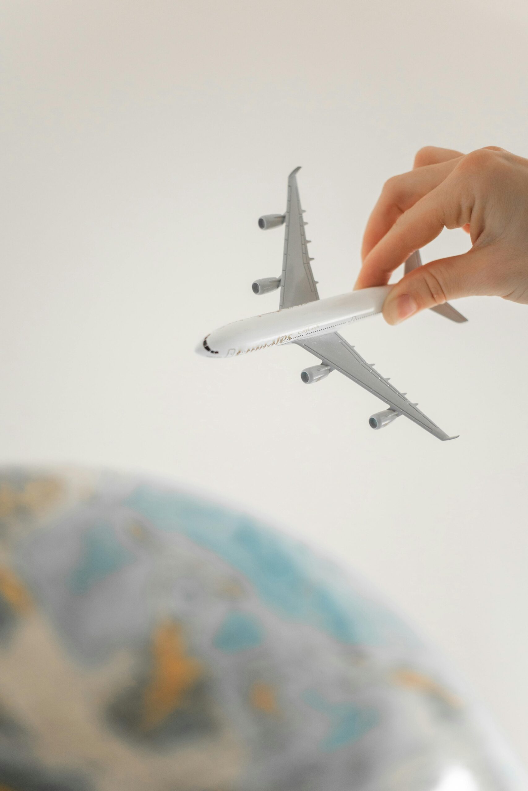 Close-up of a hand holding a toy airplane over a blurred globe, representing travel planning and adventure.
